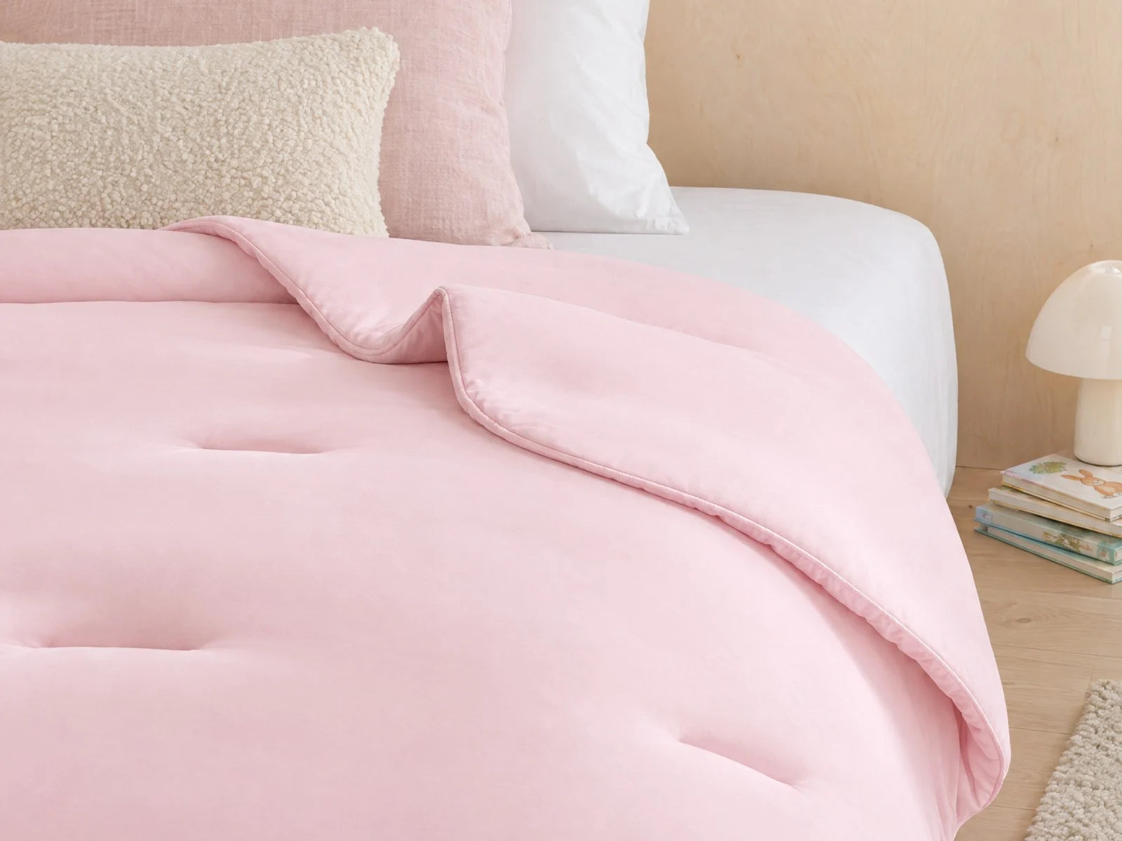 Couette Whoosh rose poudré posée sur un lit, sans housse